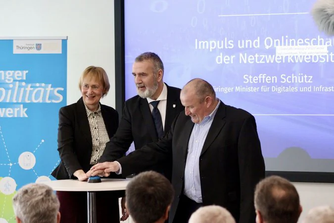 Thüringer Mobilitätskonferenz Frau Wosche (Geschäftsführung LEG), Herr Schütz (Minister des TMDI) und eine weitere männliche Person drücken vor Publikum auf einen Knopf