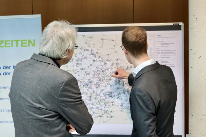 Thüringer Mobilitätskonferenz Zwei männliche Personen diskutieren an einer Pinnwand den integralen Taktfahrplan