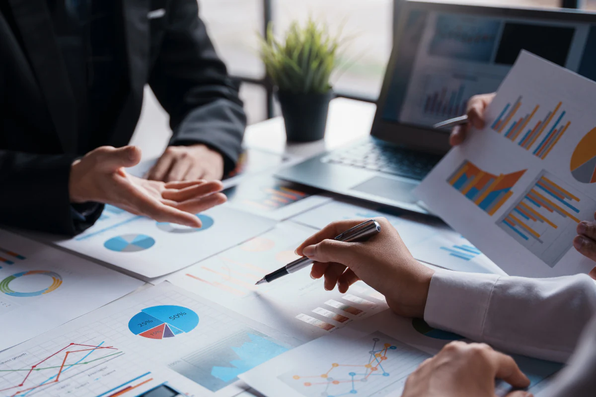 Bildbeschreibung / description: Zwei Personen analysieren gemeinsam ausgedruckte Diagramme und Grafiken am Schreibtisch; ein Laptop mit weiteren Auswertungen steht im Hintergrund.